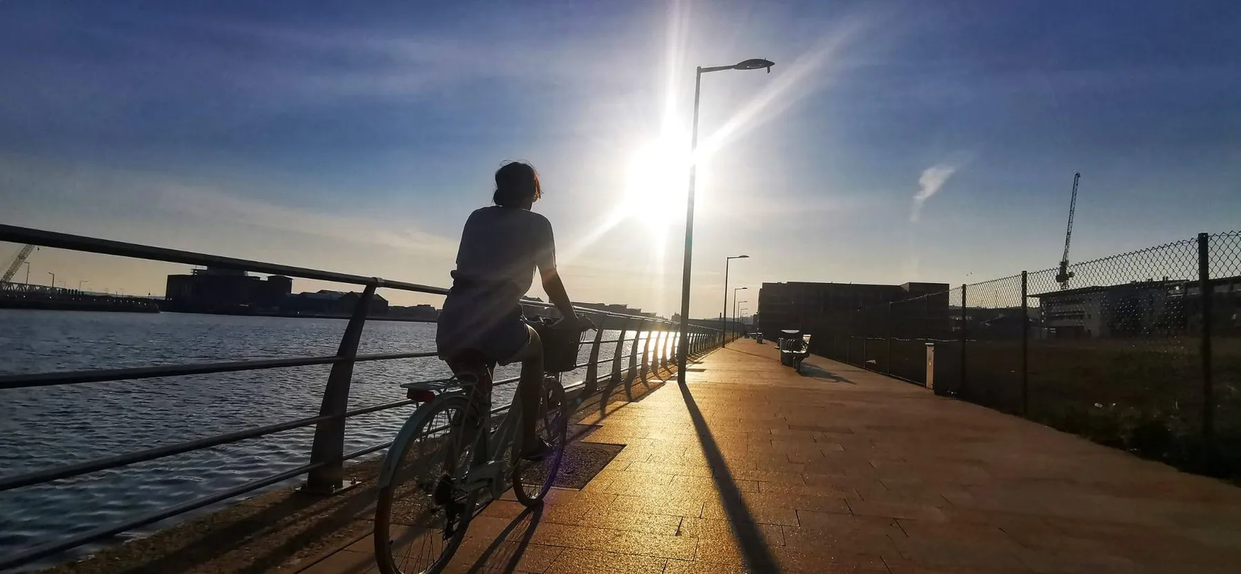 A cyclist on the promenade at Swansea Marina in low sun